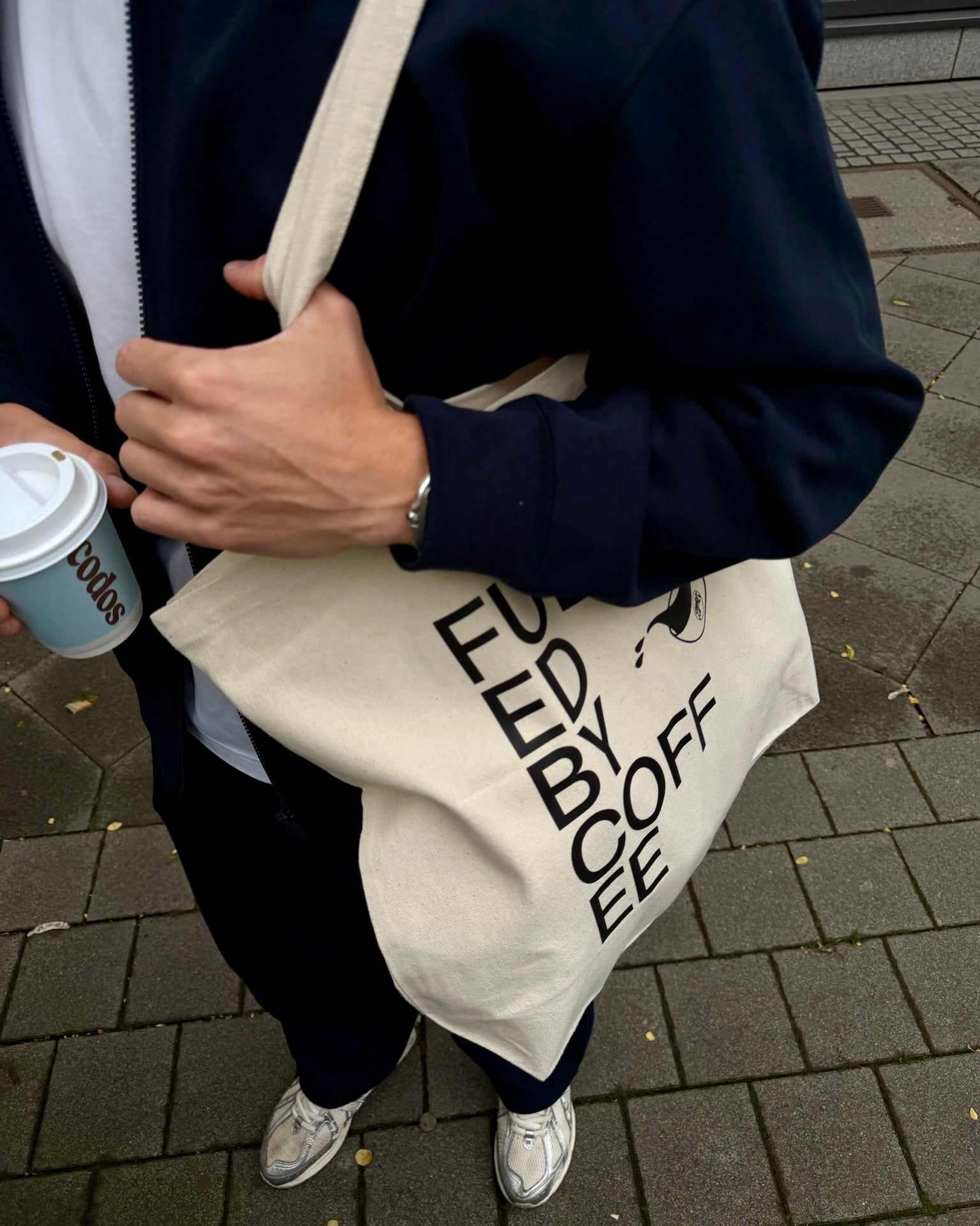 Man carrying Fuelled by Coffee Tote Outside with To-Go Coffee